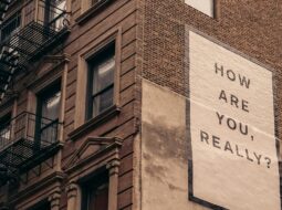 mural on the side of a brick building with fire escapes that reads, "How Are You Really?"