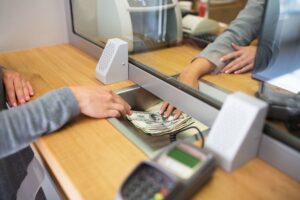 Person handing cash to a bank teller through a service window.