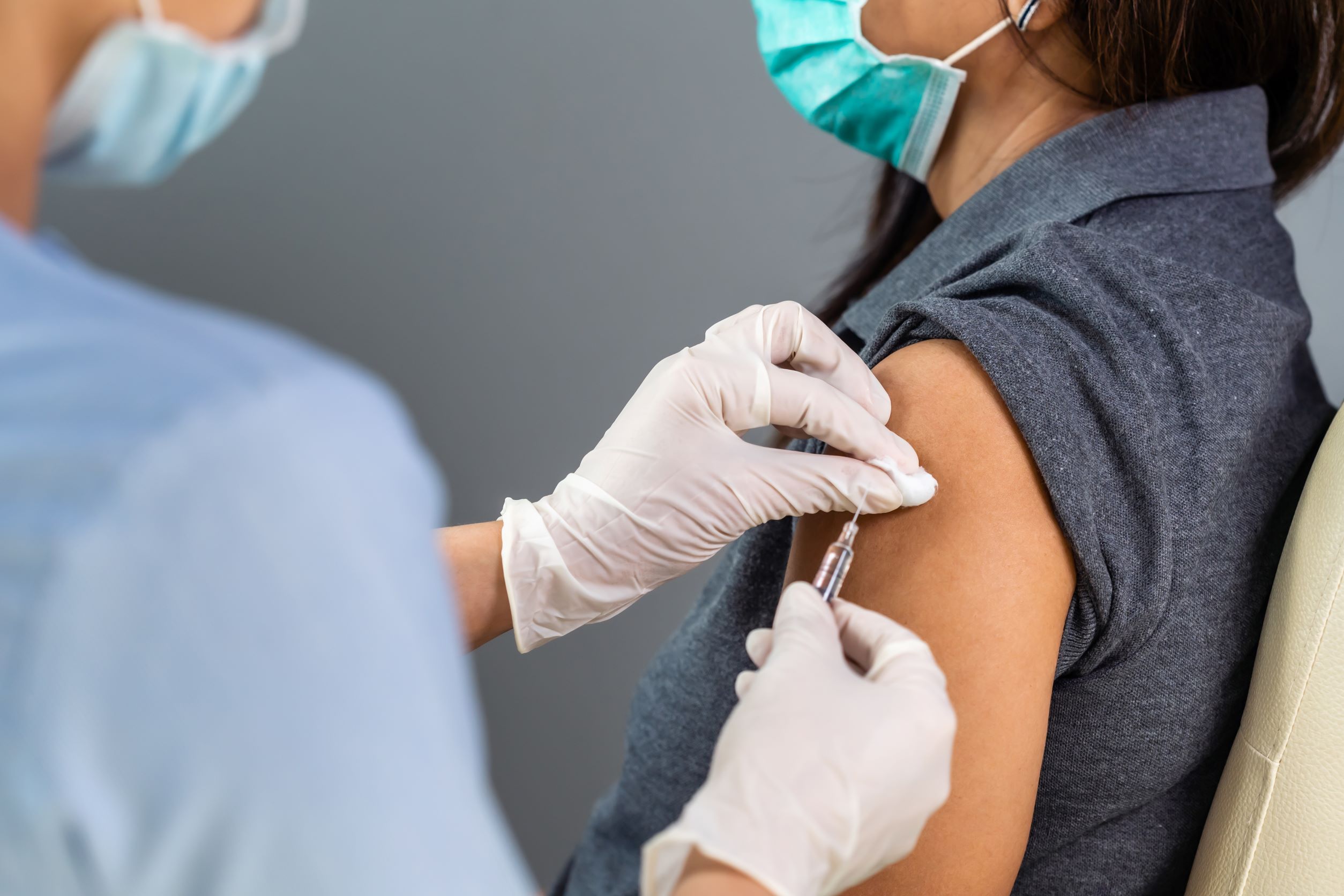 Healthcare worker administering a vaccine to a masked adult.