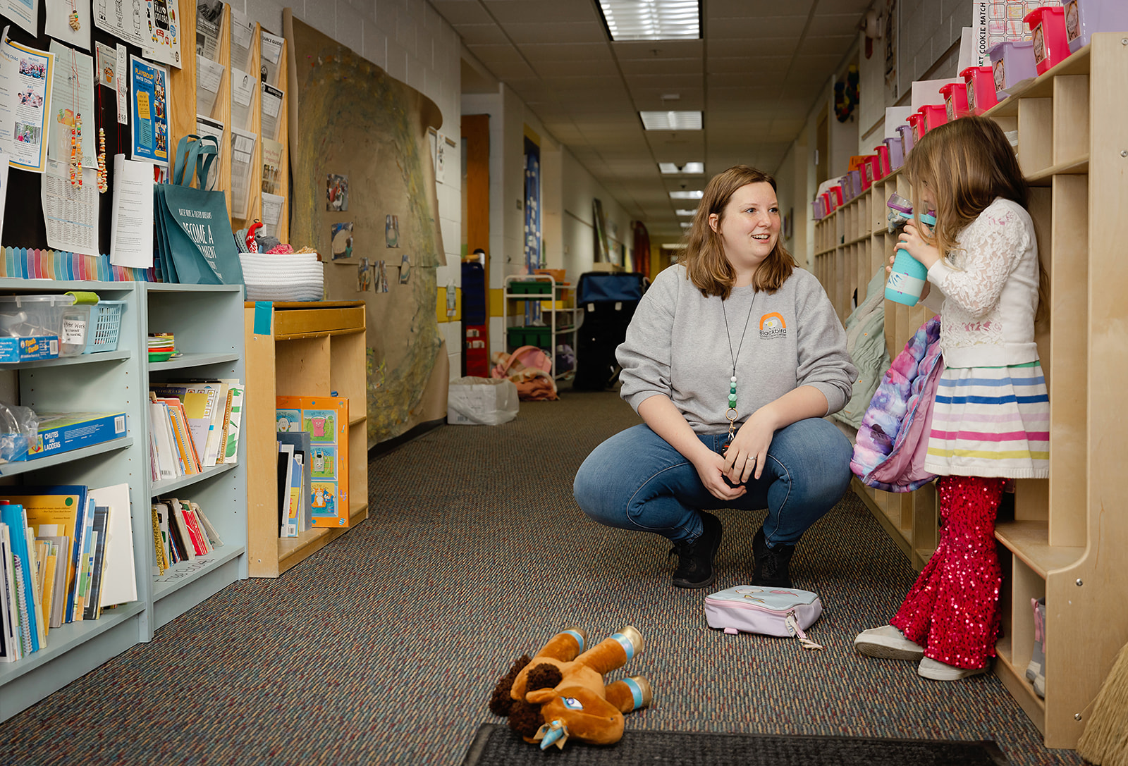Staff member talking with children in a hallway.